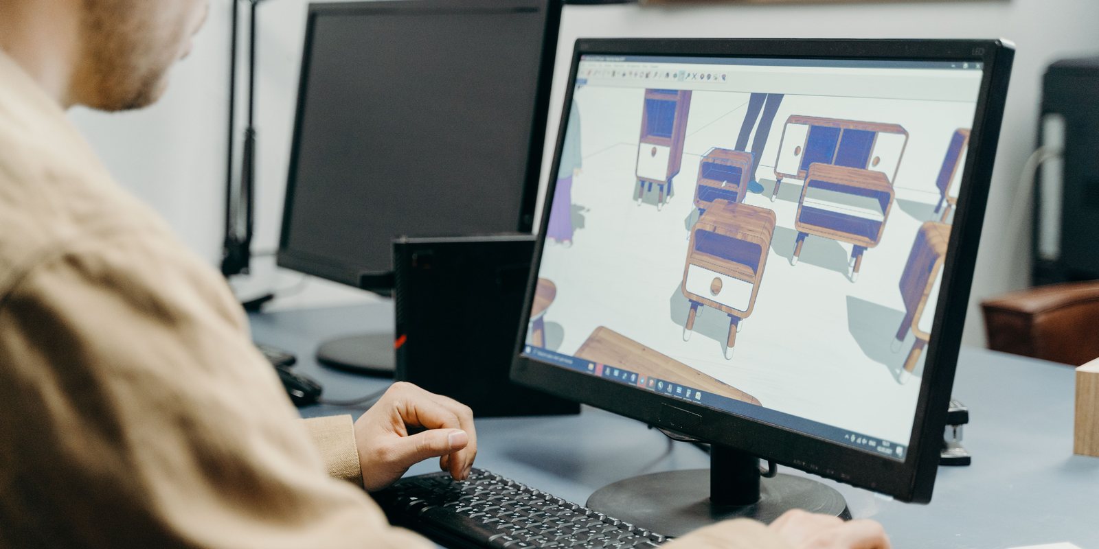 A designer at a desk works on a monitor showing 3D models of cabinets and sideboards in several sizes