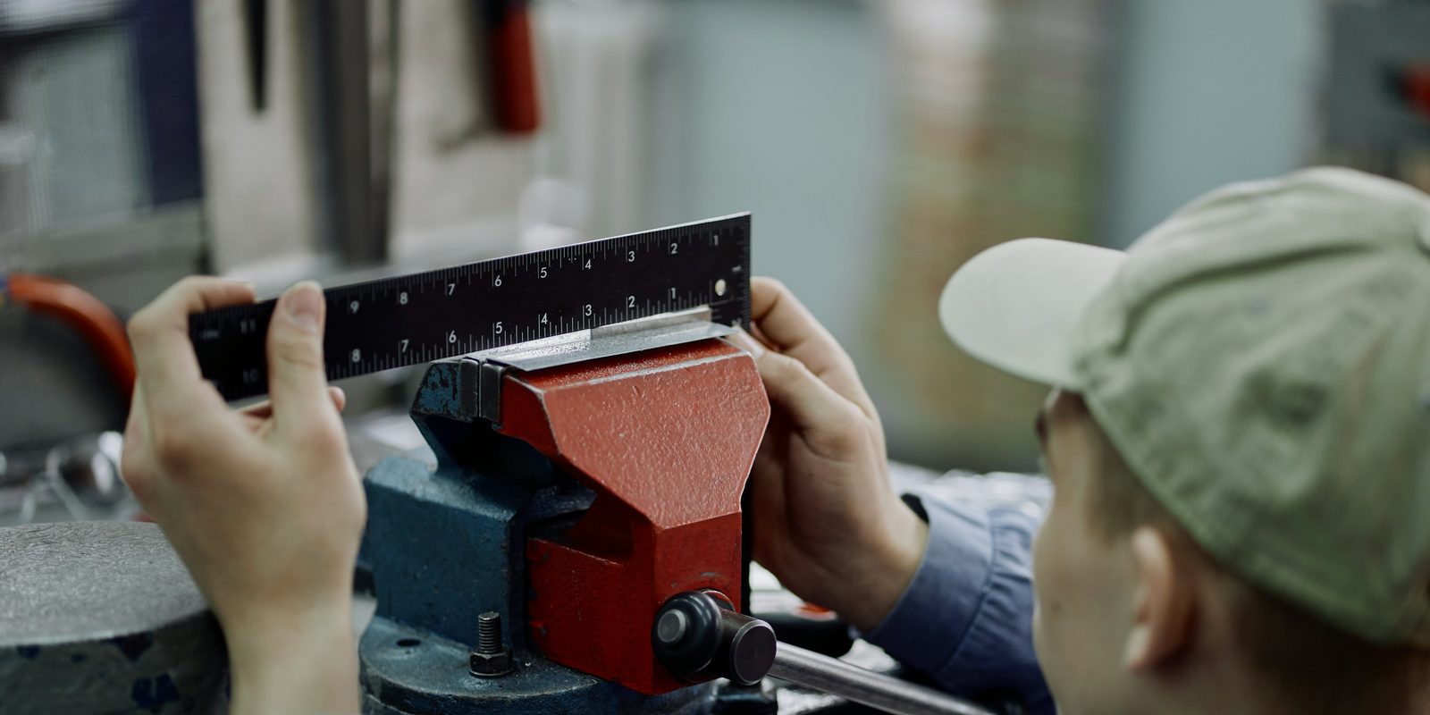 A machinist checks a steel part held in a red vise with a precision square
