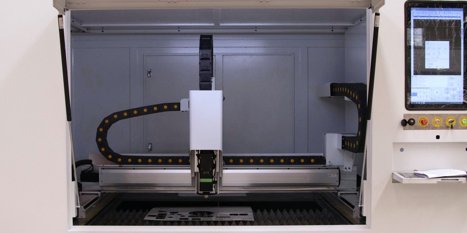 An enclosed CNC laser cutting machine with its control screen in a bright, clean shop