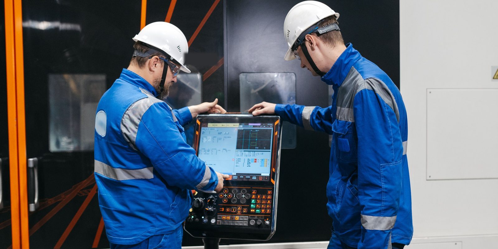 Two machinists in hard hats review a program on the touchscreen control of a CNC turning centre