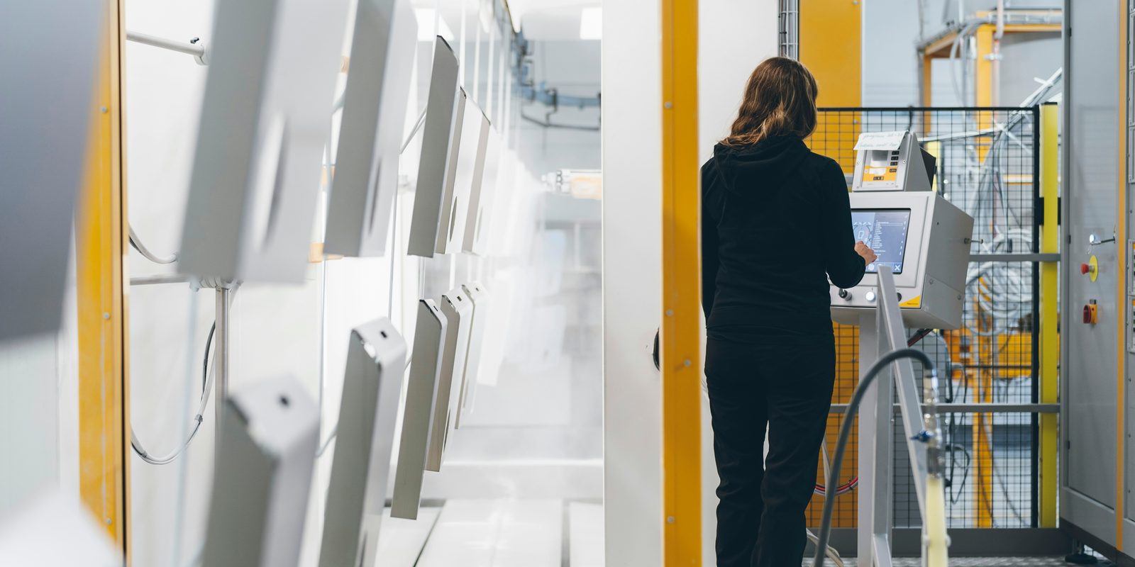 An operator works the touchscreen of an automated coating line in a bright white booth