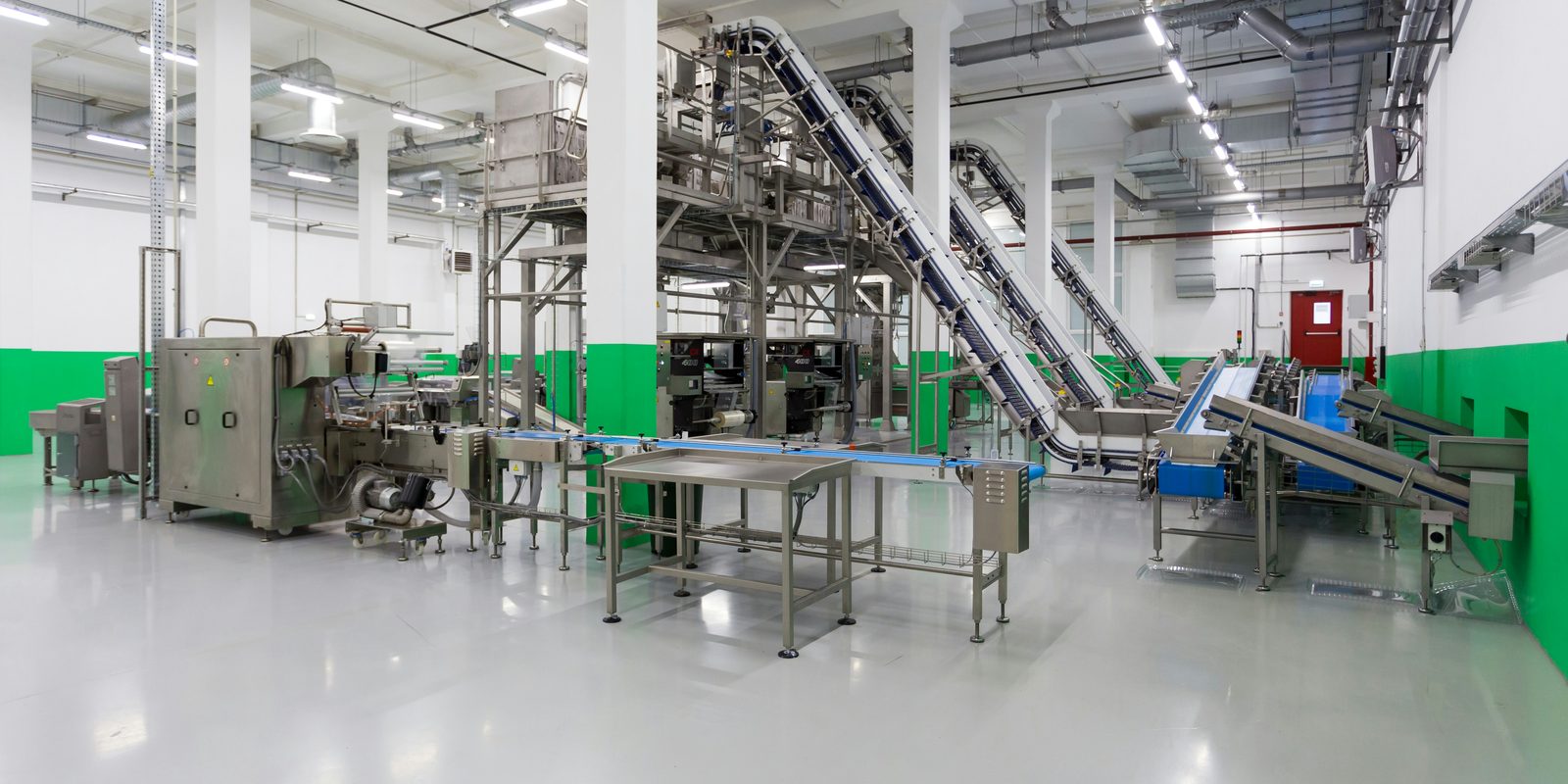 Clean, white production hall with stainless processing machines and inclined conveyors, no people