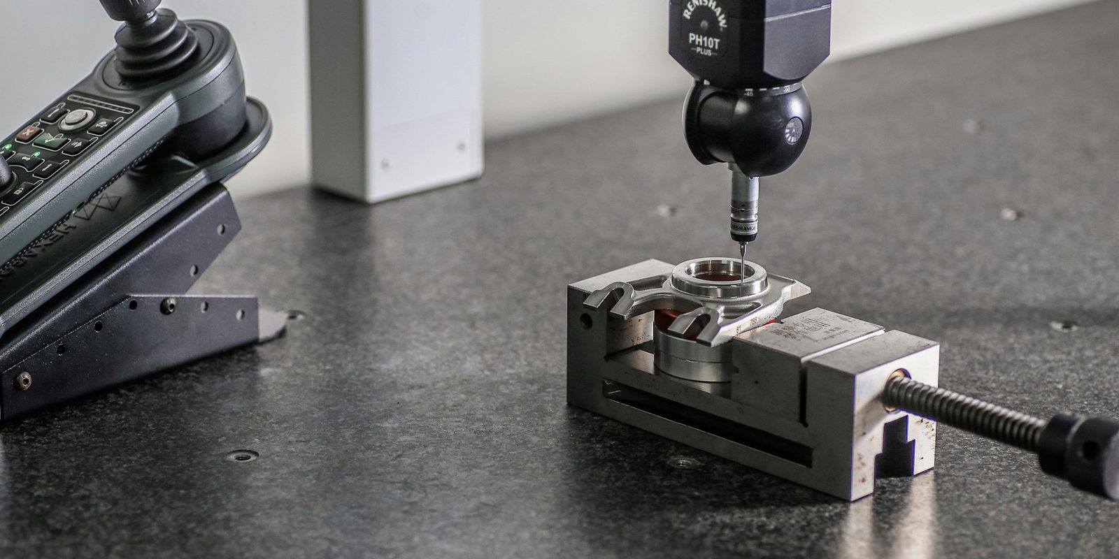 A coordinate measuring machine probe touching a machined part held in a precision vise on a granite table