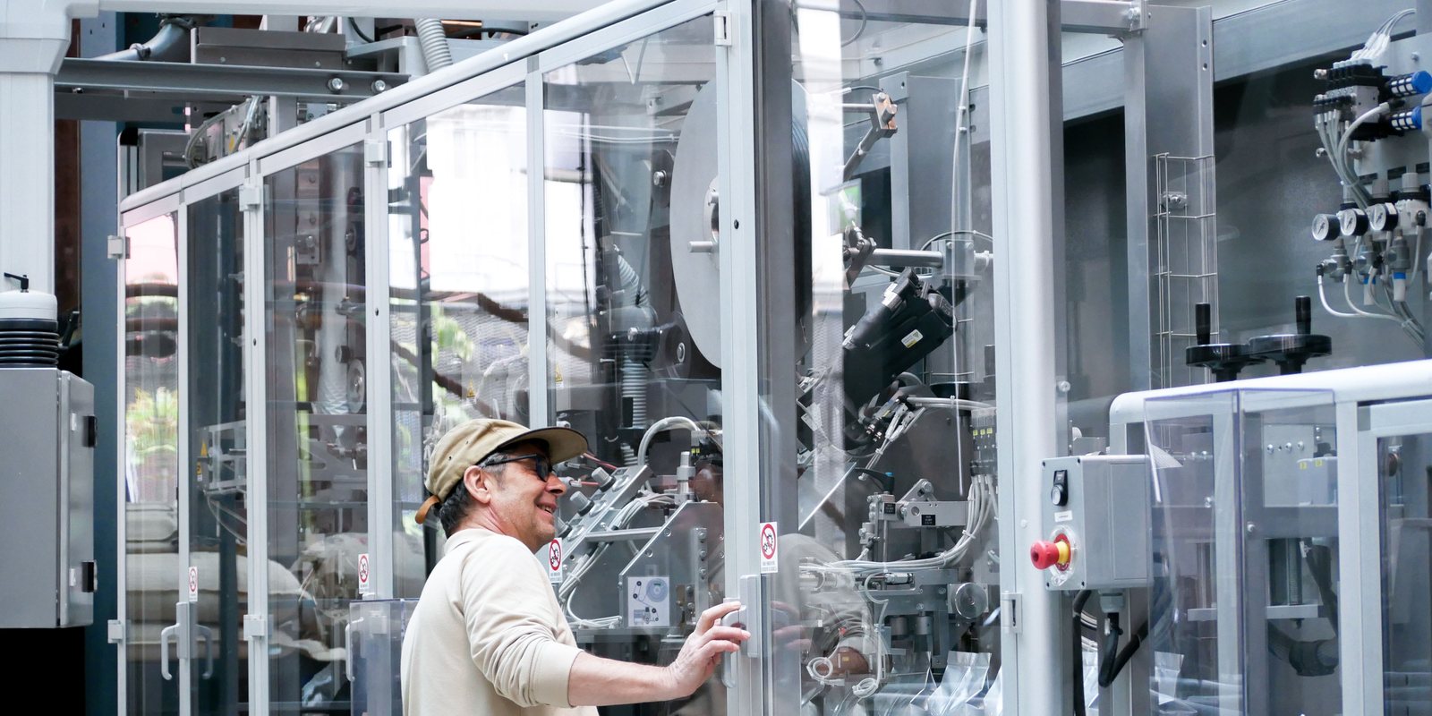 A technician checks an automated packaging machine behind clear safety guards on a factory floor